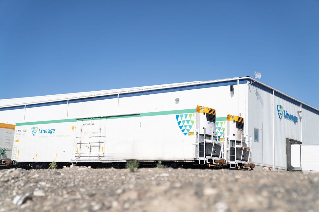 Vagones Lineage situados junto a unas instalaciones de almacenamiento con control de temperatura, que dan soporte a las operaciones de transporte y almacenamiento de la cadena de frío.