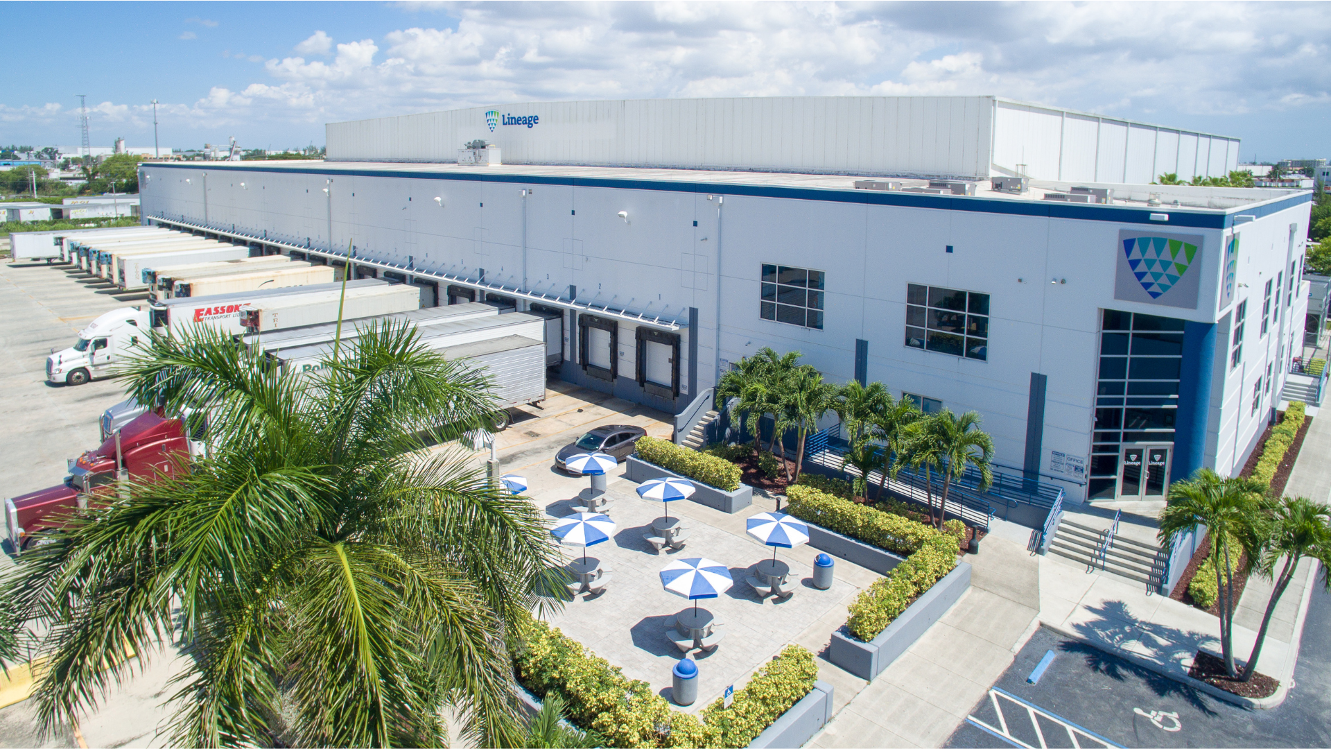 Vue aérienne de Lineage entrepôt frigorifique à Miami présentant le vaste entrepôt, les quais de chargement avec camions et l’espace extérieur paysager avec des sièges ombragés.