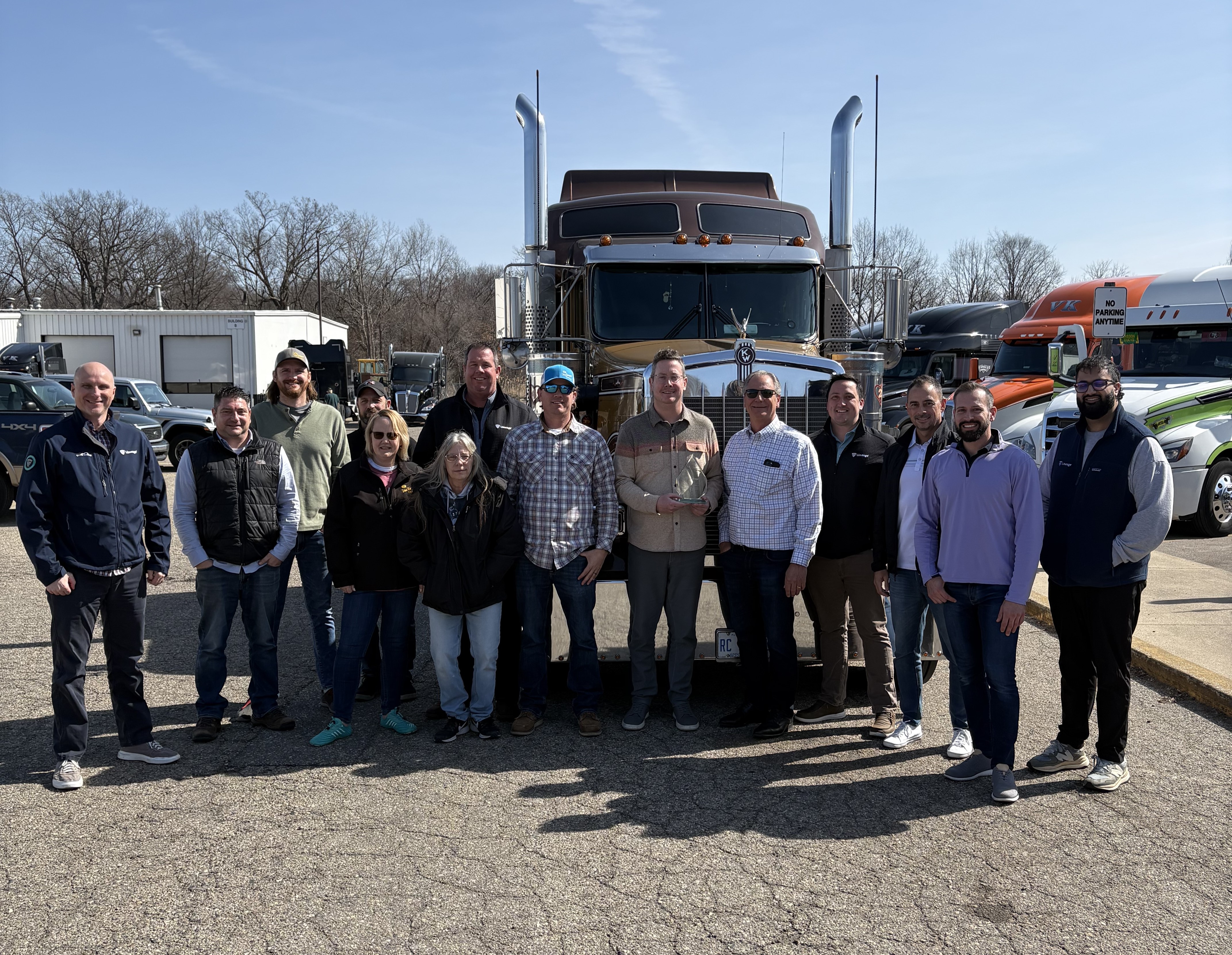 Un grupo de representantes de MC Van Kampen Trucking delante de un semirremolque tras recibir el premio al Transportista del Año de Lineage.
