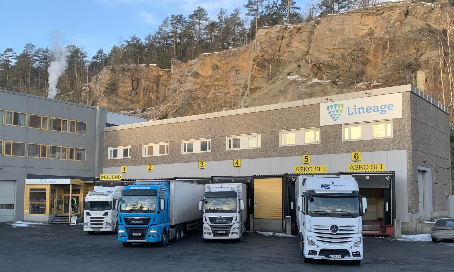 Almacén frigorífico de Lineage en Moss (Noruega), construido en una ladera rocosa con semirremolques en los muelles de carga y vapor saliendo por detrás.