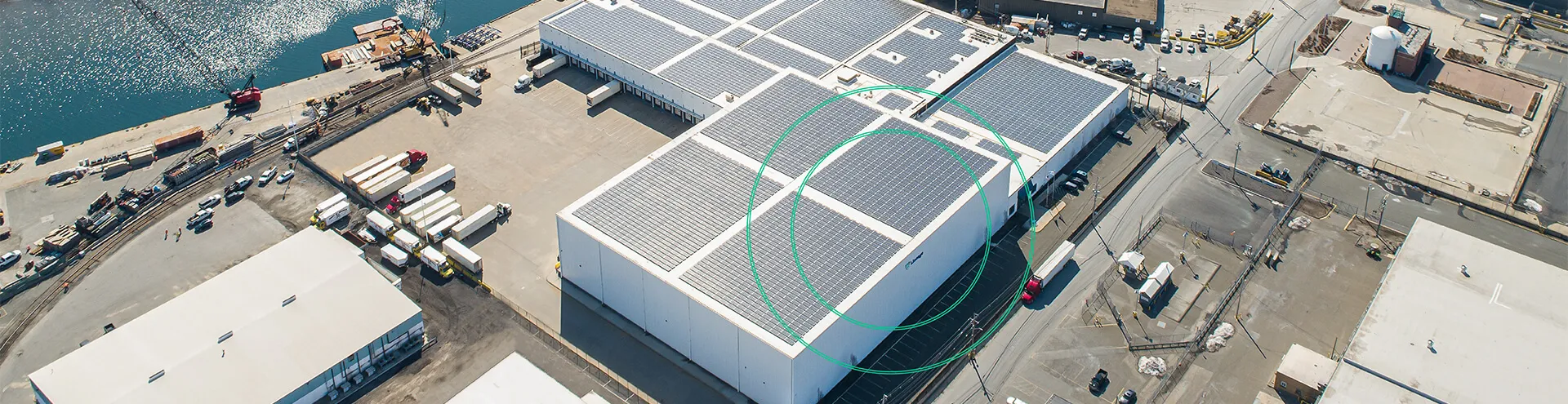 Aerial view of a Lineage cold storage facility in the Northeast U.S. featuring rooftop solar panels, with nearby highways and port infrastructure visible in the background.