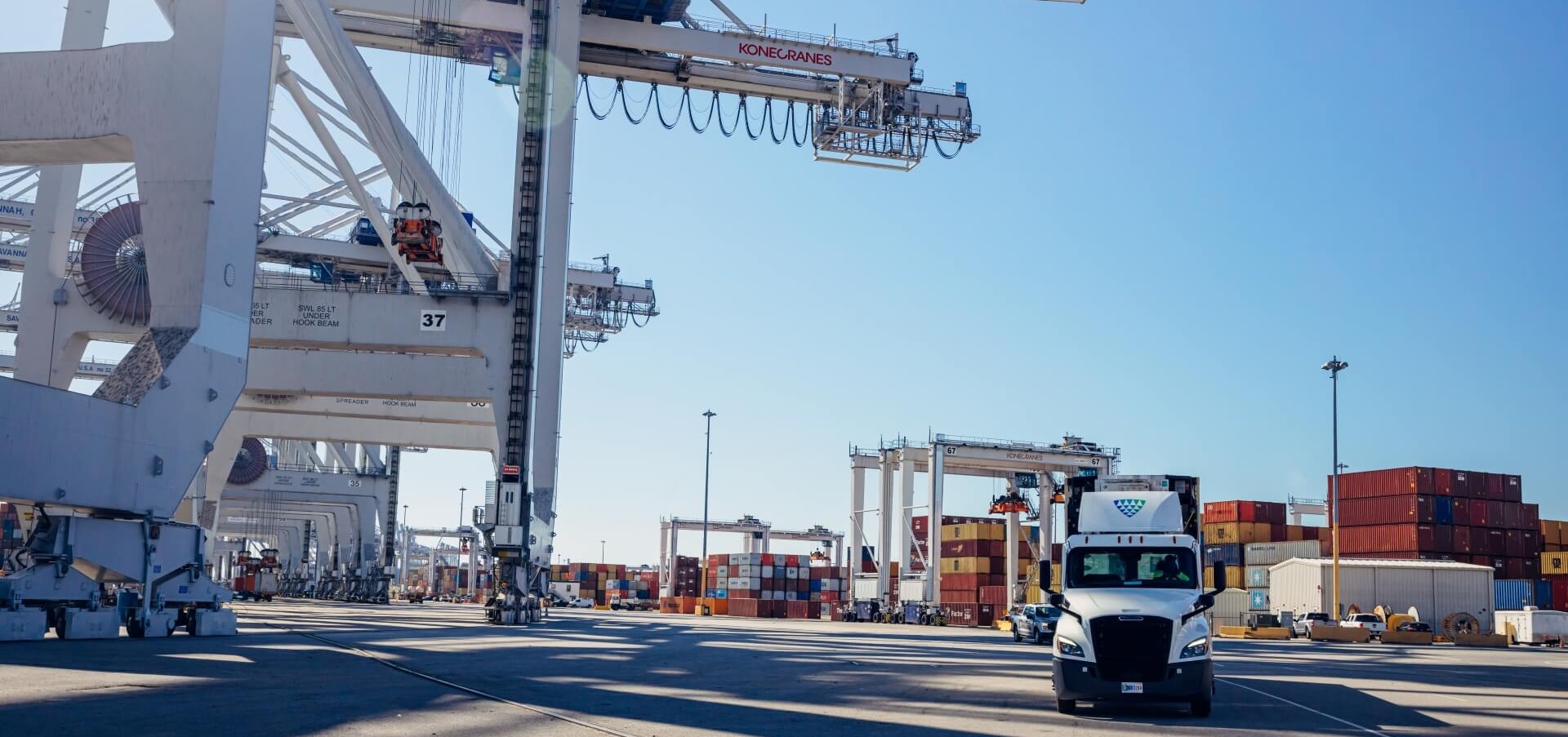Lineage truck driving through a container port surrounded by cranes and stacked shipping containers, highlighting import/export and drayage operations