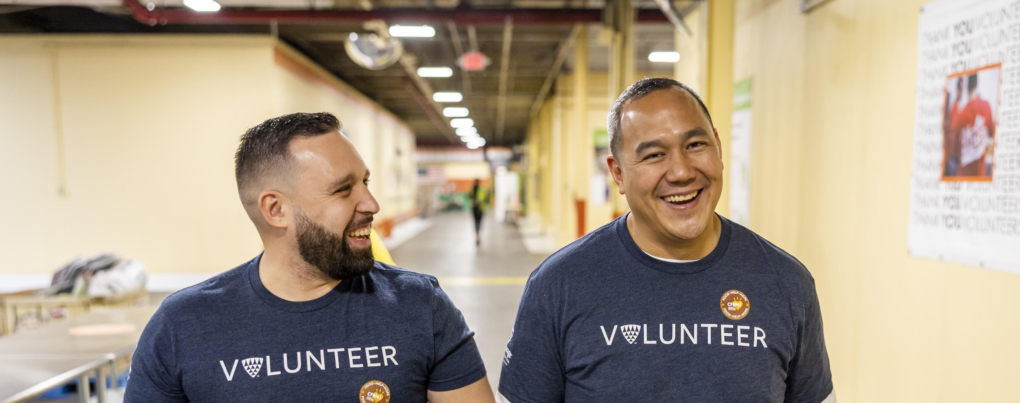 Two Lineage team members wearing “Volunteer” shirts walk together through a warehouse facility, smiling during a community volunteer event.