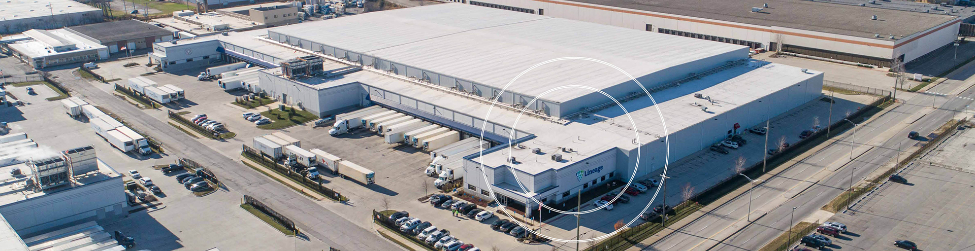Aerial view of a Lineage cold storage facility in the Midwest, showing warehouse buildings, loading docks, parked trailers and surrounding road and rail access.