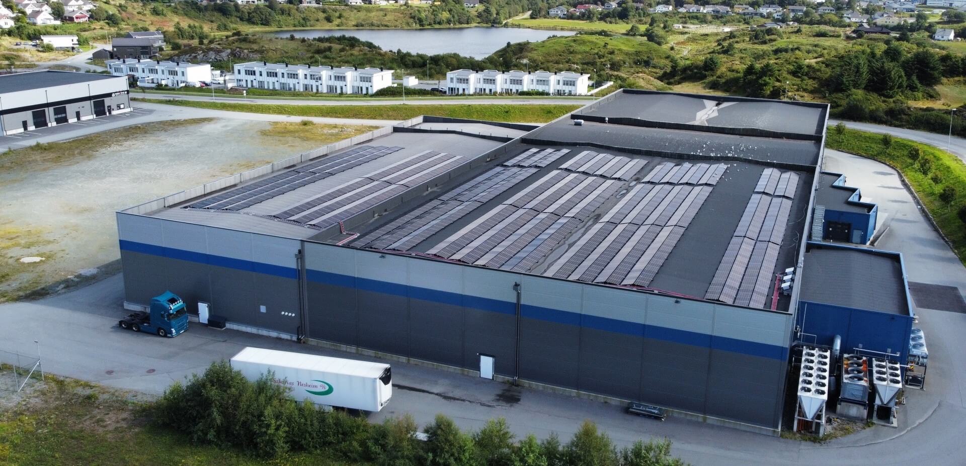 Aerial view of the Lineage cold storage facility in Haugesund, Norway, featuring rooftop solar panels, loading areas and surrounding residential and natural landscapes.