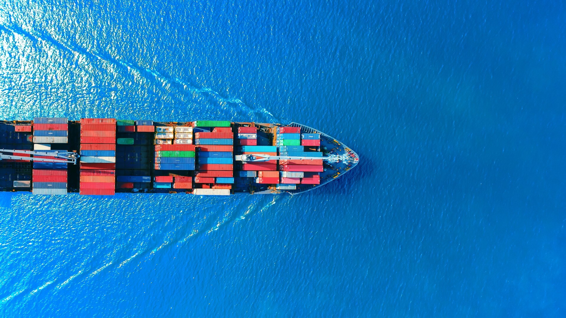 Aerial view of a cargo ship transporting shipping containers across the ocean, illustrating international trade, ocean freight and global supply chain logistics.