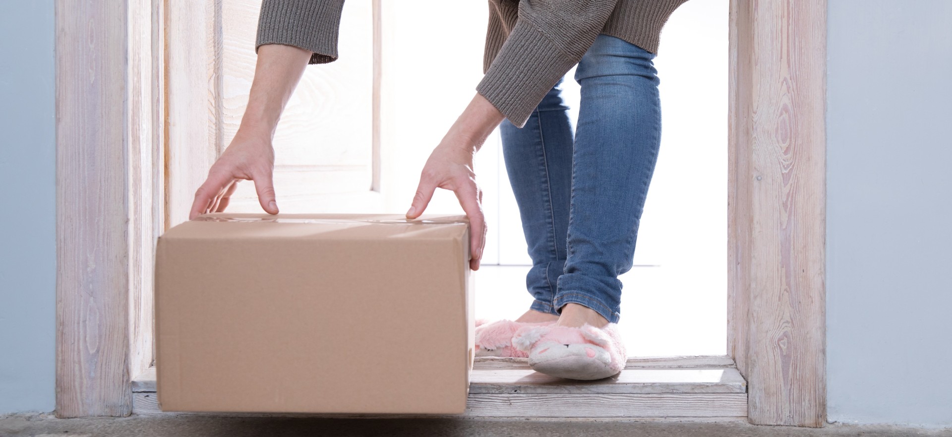Person receiving a cardboard delivery box at their doorstep, representing direct-to-consumer fulfillment and home delivery.