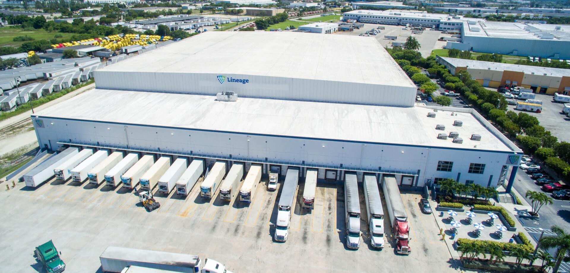 Aerial view of a Lineage cold storage warehouse with refrigerated trucks and trailers positioned at loading docks.