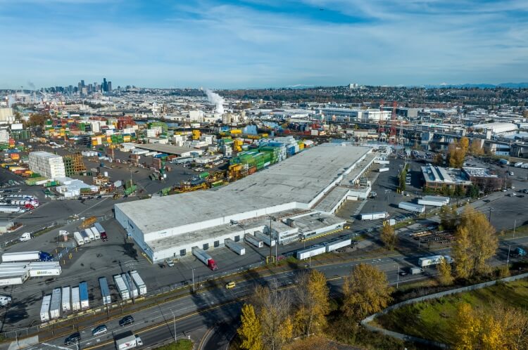 Vista aérea de las instalaciones de Lineageen Seattle-Michigan con el horizonte de Seattle al fondo, destacando su ubicación estratégica cerca de la logística portuaria y urbana.