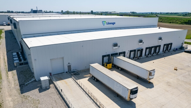 Lineage cold storage facility in Canada with loading docks and refrigerated trailers, showcasing infrastructure for food logistics and distribution.