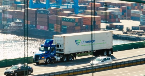 Lineage refrigerated truck transporting goods past a container port, highlighting cross-border logistics and freight movement