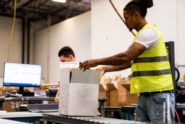 Lineage team member packing a direct-to-consumer order at a fulfillment station while another team member works nearby.