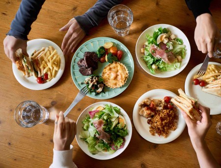 Overhead view of a shared meal with multiple plates of food on a table, highlighting the connection between food consumption, waste awareness and food system impact.