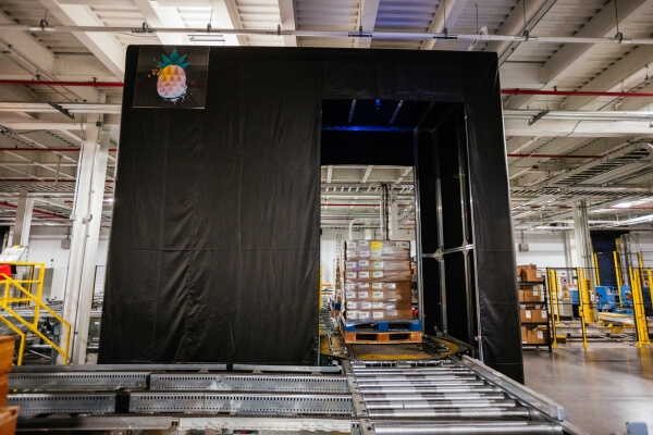 A neatly stacked pallet positioned on a Lineage Eye conveyor system in a clean, well-organized, automated cold storage warehouse, with safety guardrails and scanning stations in the vicinity.