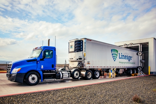 Lineage refrigerated trailer backed into a cold storage dock, with a blue truck and team members loading product for temperature-controlled delivery.