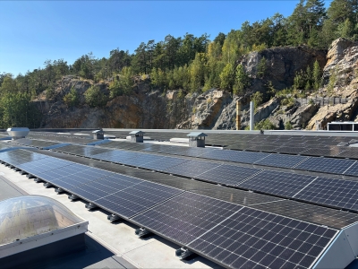 Rooftop solar panels at the Lineage cold storage facility in Moss, Norway, surrounded by forested cliffs and clear blue skies.