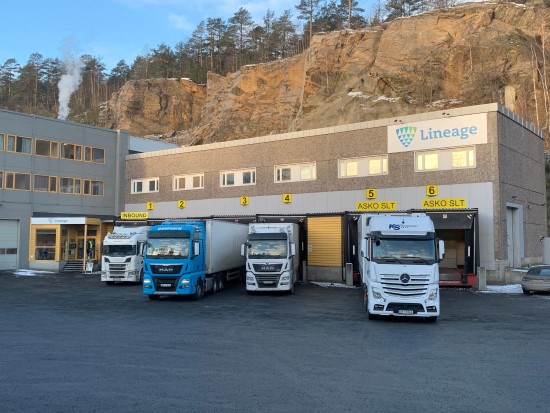 Trucks parked outside the Lineage cold storage facility in Moss, Norway, which is built into a rocky hillside and serves as a temperature-controlled warehouse with multiple loading bays.
