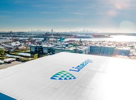 Aerial view of a Lineage cold storage warehouse near the Port of New York and New Jersey, with the city skyline and waterfront in the background.