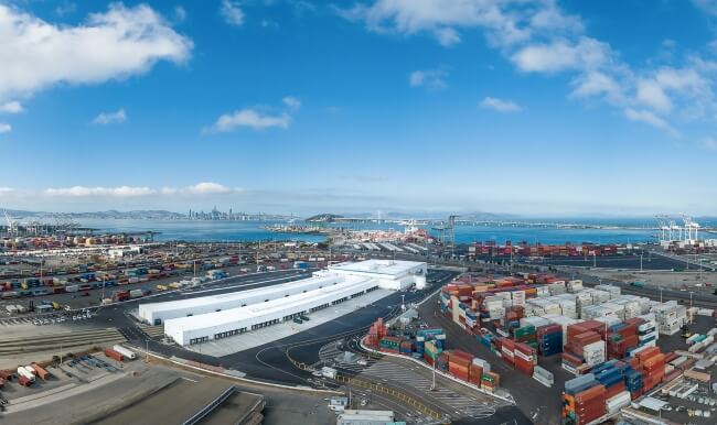 Panoramic view of a busy container port with a Lineage facility and drayage trucks positioned near stacked shipping containers