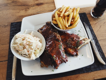 Plate of barbecue ribs with French fries and coleslaw served at a restaurant, representing the end result of an efficient foodservice supply chain.