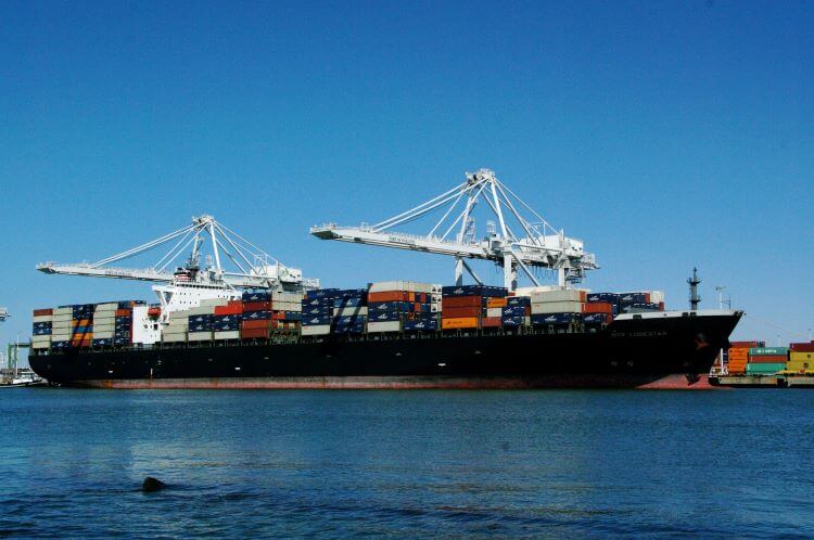 Container ship loaded with cargo docked at a port, with cranes in the background under a clear blue sky, showcasing ocean freight as a key link in the global food supply chain.