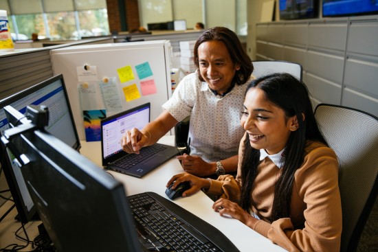 Two Lineage employees collaborate at computer workstations in an office setting, reviewing information and supporting customs brokerage and logistics operations.