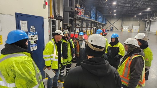 Los miembros del equipo Lineage , con equipos de alta visibilidad y cascos, se reúnen para una reunión de seguridad en el almacén de Calgary.