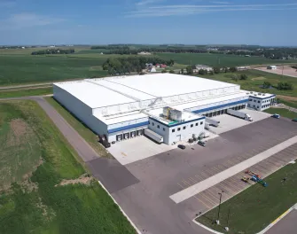 Aerial view of Lineage's Luverne cold storage warehouse in Minnesota, featuring multiple loading docks, parked trailers, and expansive surrounding farmland, highlighting its strategic location for cold chain operations.