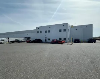 Exterior view of Lineage's Pasco cold storage warehouse in Washington, featuring a modern white facility with parked trucks, cars, and spacious lot for logistics operations.