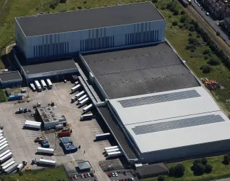 Vue aérienne de LineageEntrepôt frigorifique et installation portuaire de Grimsby, au Royaume-Uni, avec des quais de chargement, des panneaux solaires et des remorques réfrigérées.