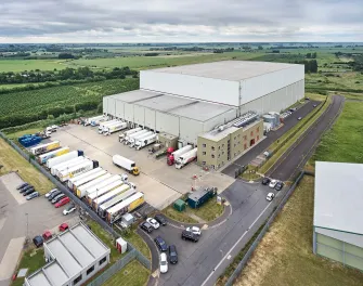 Vue aérienne de LineageEntrepôt frigorifique automatisé Wisbech – Boleness au Royaume-Uni, avec plusieurs camions sur les quais de chargement.
