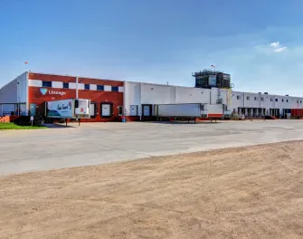 Vue extérieure de la Lineage installation de stockage frigorifique à Friona, Texas, avec l’entrepôt en brique et blanc, les quais de chargement et les remorques sous un ciel dégagé.