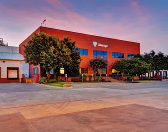 Extérieur de la Lineage à Fort Worth, Texas, avec le bâtiment de bureaux rouge, les quais de chargement et les arbres environnants au crépuscule.