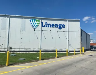 Exterior view of Lineage’s Houston Hwy 225 facility, showing the white warehouse wall with the Lineage logo, yellow safety bollards and a clear blue sky.