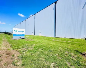 Exterior of Lineage’s Cold Port facility in Houston, Texas, showing the large white warehouse wall and the Lineage sign along the grassy front lawn on a clear day.
