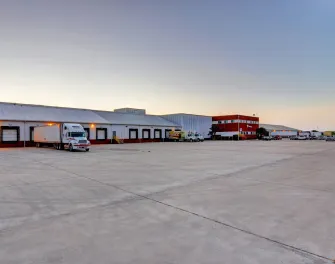 Vue large de Lineagede McAllen South Ware, montrant les quais de chargement, les camions et l’immeuble de bureaux rouge au crépuscule.