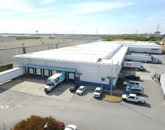 Vue aérienne de LineageSan Antonio Frost Bank Center, montrant l’entrepôt blanc, les quais de chargement, les remorques et les véhicules stationnés par une journée claire.