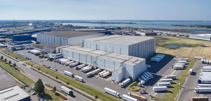 Vue aérienne de Lineage's Bergen op Zoom, installation d’entreposage frigorifique aux Pays-Bas, comprenant plusieurs quais de chargement et camions réfrigérés pour le factage et la distribution.