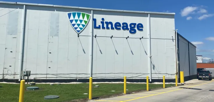 Exterior view of Lineage’s Houston Hwy 225 facility, showing the white warehouse wall with the Lineage logo, yellow safety bollards and a clear blue sky.
