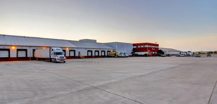 Wide view of Lineage’s McAllen South Ware facility, showing the loading docks, trucks and the red office building at dusk.