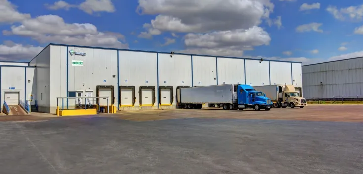 Exterior of Lineage’s McAllen West Military facility, showing the white warehouse with multiple loading docks and several trucks parked under a partly cloudy sky.
