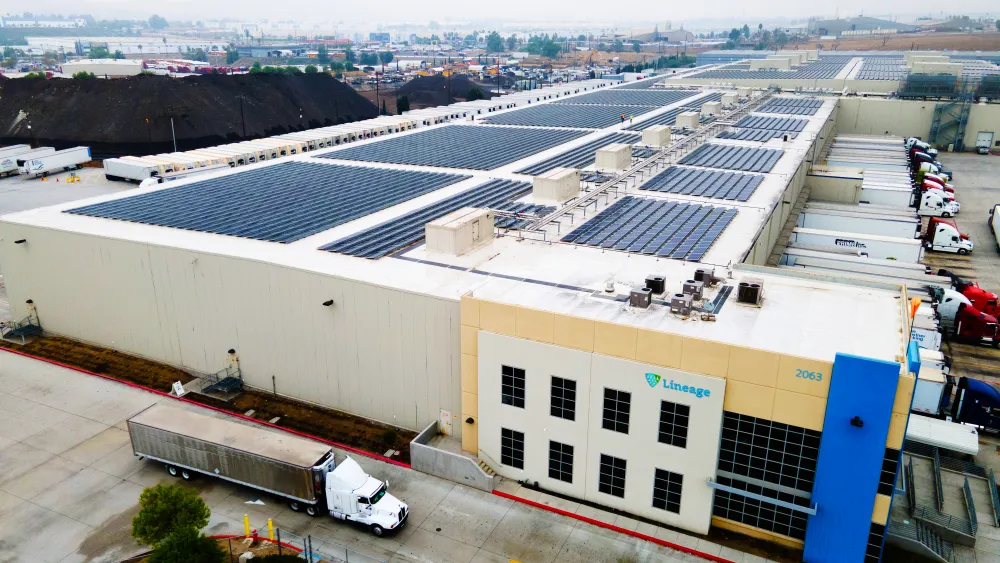 Vue aérienne d’un Lineage Entrepôt frigorifique doté de panneaux solaires sur le toit et d’une flotte de camions prêts pour les services de transport.