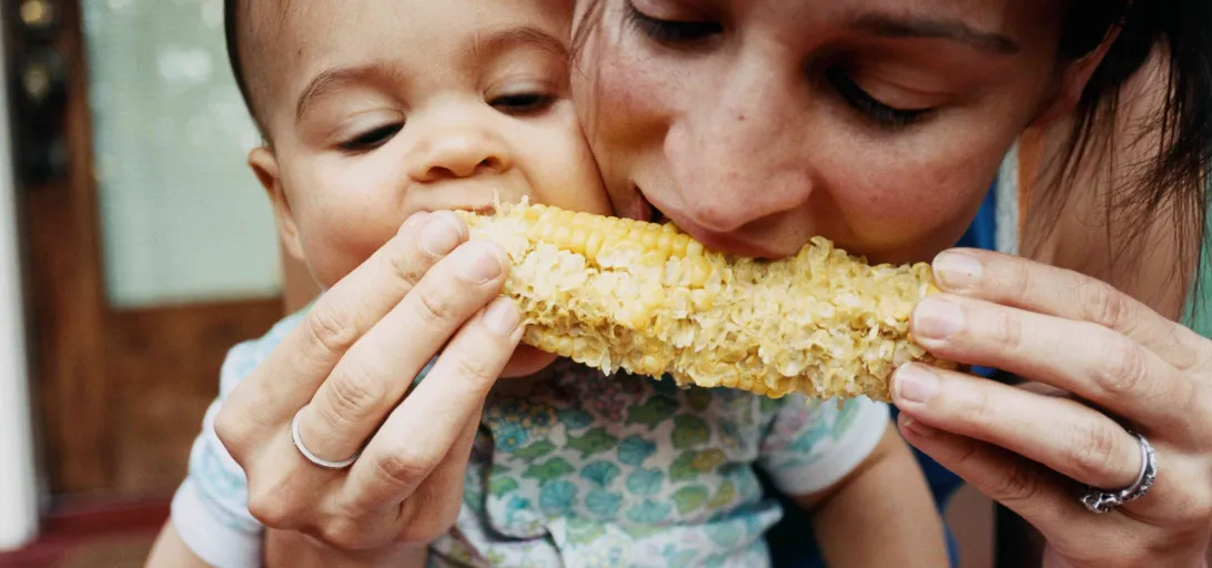 A mother and young child share corn on the cob