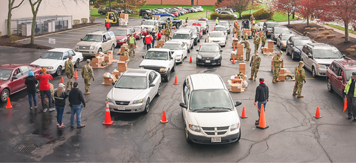 Cars in lines receiving food from soldiers and civilians