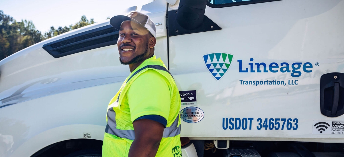 Smiling driver in high-visibility vest standing beside a Lineage Transportation truck, representing the dedicated workforce behind efficient food supply chain logistics.