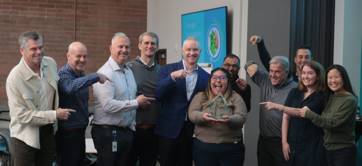 Swemy Sanchez Roman, holding her Servant Leader for Good award, beams with pride as her colleagues at Lineage celebrate her achievement, pointing and smiling in recognition of her dedication to community service and leadership.