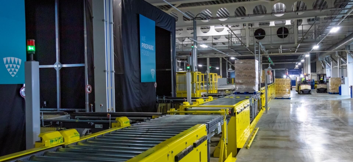 A modern cold storage warehouse featuring yellow conveyor systems and forklifts moving pallets. Lineage Eye automation streamlines receiving and inventory management.