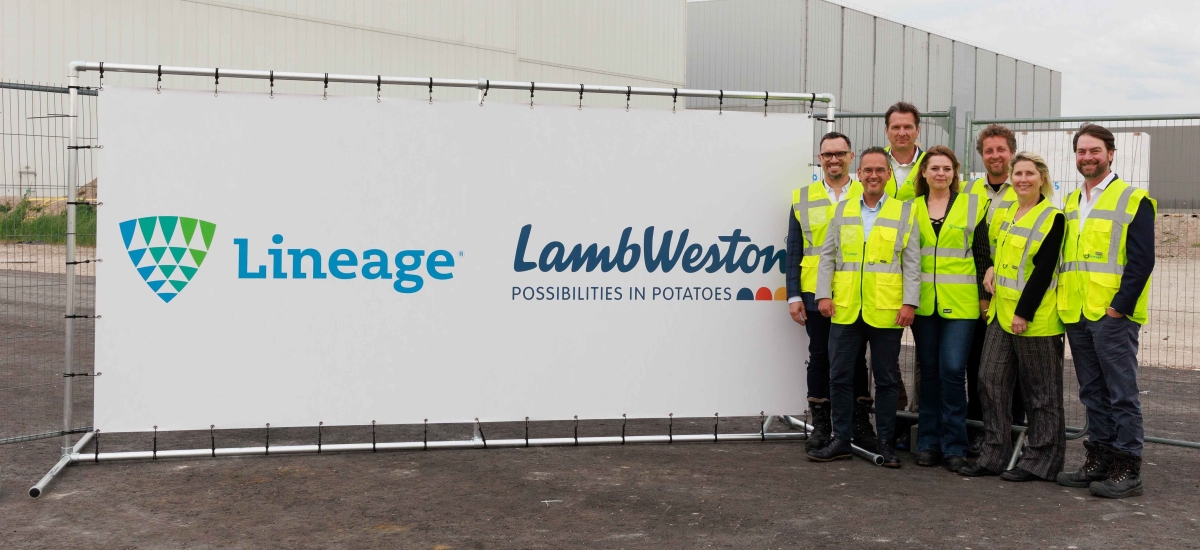 A group of people in high visibility gear stand near a sign announcing Lineage's expansion with customer Lamb Weston