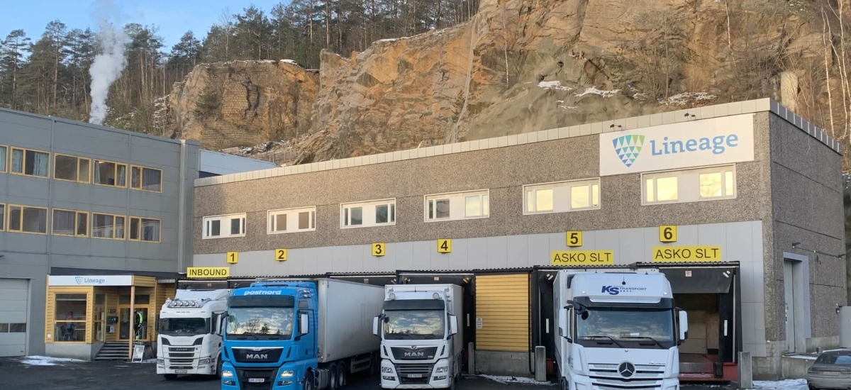 Lineage cold storage facility in Moss, Norway, built into a rocky hillside with semi-trucks at the loading bays and steam rising from behind the site.