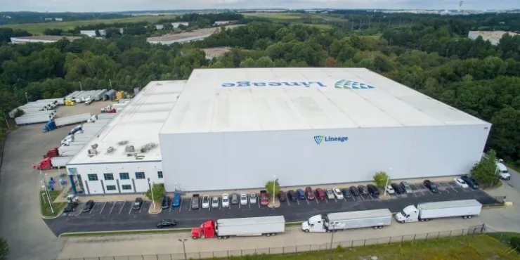 Vista aérea de las instalaciones de almacenamiento en frío de Lineage en College Park, Atlanta (GA), con un gran almacén, varias bahías para camiones, remolques aparcados y el paisaje verde circundante, que pone de relieve la avanzada infraestructura logística.